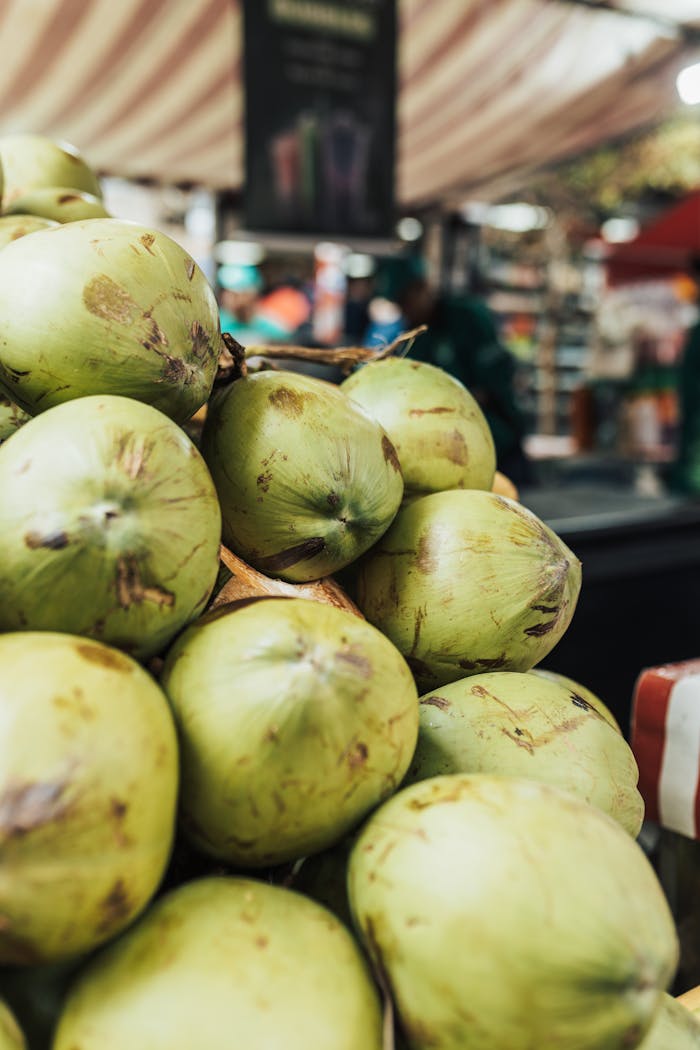 Close-up of fresh green coconuts stacked in a vibrant outdoor market setting.