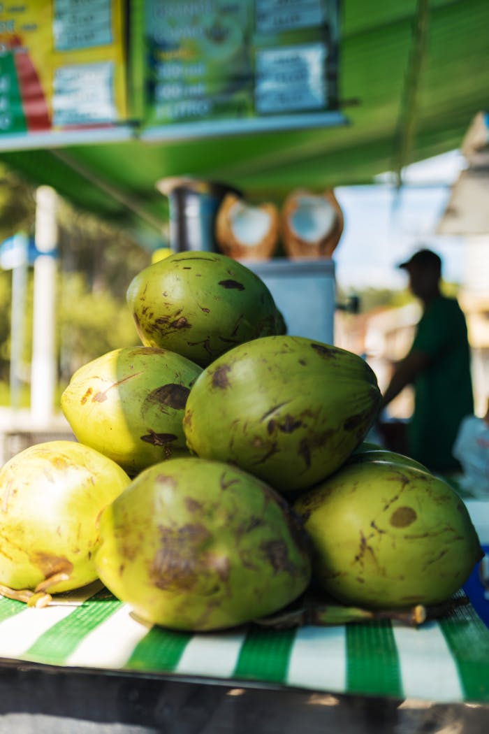 A vibrant display of green coconuts at an outdoor market with a vendor in the background.