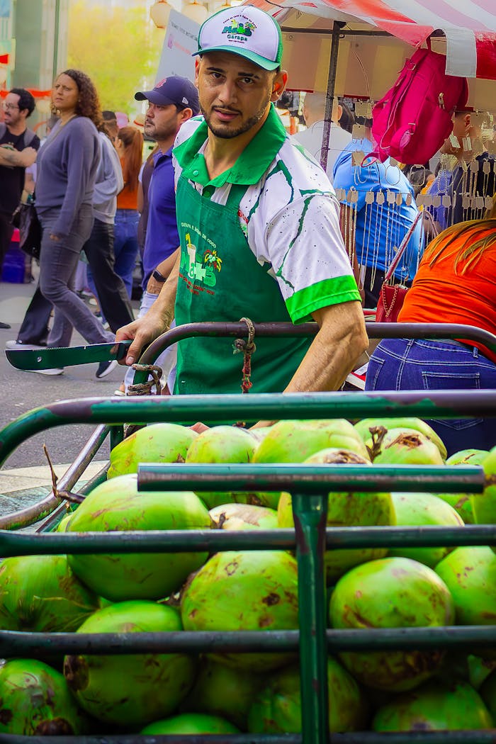 A lively market scene with a street vendor selling fresh green coconuts to passersby.